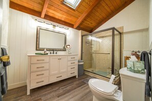 Un baño con techo de madera, un espejo grande, cabina de ducha y un inodoro.