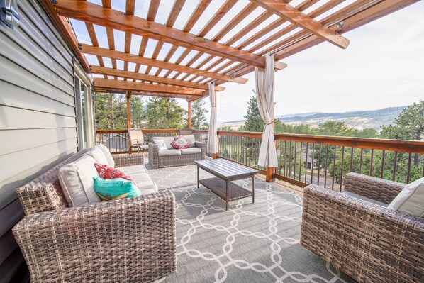 Un espacio de estar al aire libre con techo, muebles de mimbre, una mesa y vistas al paisaje.