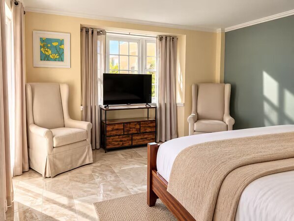 A hotel room with a bed, two armchairs, a TV on a wooden stand, and a window with curtains.