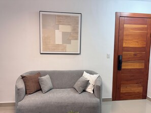 A grey sofa with cushions, a wooden door, and a framed abstract artwork on the wall. - Brand-New Modern Retreat in Sosúa (Sosua)