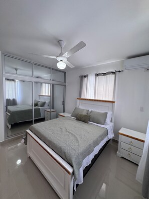 A bedroom with a bed, a nightstand, a dresser, a ceiling fan, and a window with curtains. - Brand-New Modern Retreat in Sosúa (Sosua)