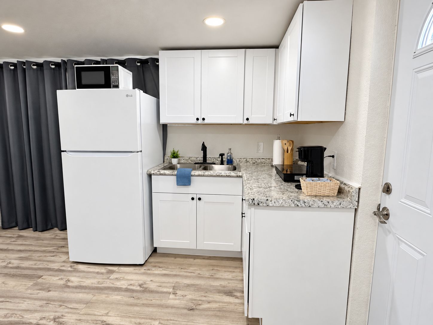 A compact kitchen with white cabinets, a built-in microwave, a sink, and a coffee maker.