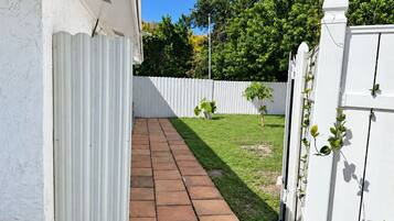 A paved pathway leading to a white fence with a small tree and potted plants.