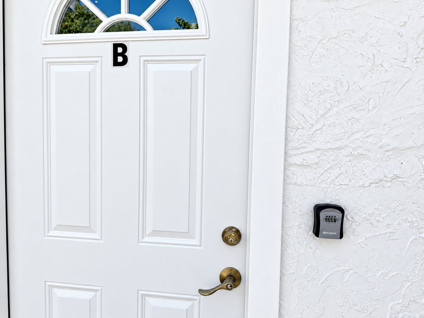 A white door with a window above it, a brass door handle, and a doorbell with the brand name 'GIVERARE' on the wall beside it.