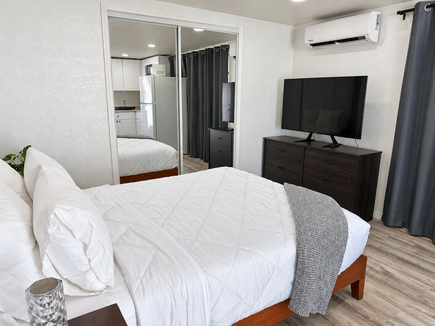 Un dormitorio con una cama, un televisor, un armario y un equipo de aire acondicionado.