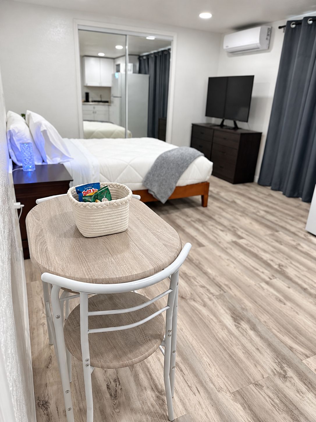 A hotel room with a bed, a television, a desk with a chair, and a small table with a basket.