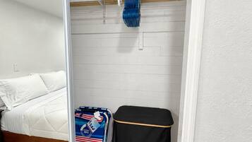 A room with a bed, a suitcase, a small black ottoman, and a blue suitcase with red and white stripes.