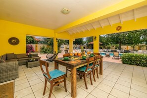 A bright yellow covered patio with a dining table set for four, surrounded by wicker furniture and chairs with blue cushions. - SunnyStay Villa - A Spacious 5-Bedroom Villa with Pool & Mini Golf (Moko)