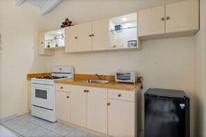 A compact kitchen with a gas stove, oven, a black refrigerator, and a toaster. - SunnyStay Villa - A Spacious 5-Bedroom Villa with Pool & Mini Golf (Moko)