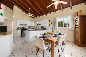 A spacious kitchen with white cabinets, a central island, and a dining area with a wooden table and chairs. - SunnyStay Villa - A Spacious 5-Bedroom Villa with Pool & Mini Golf (Moko)
