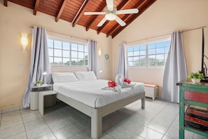 A bedroom with a bed, two bedside tables, a nightstand, a ceiling fan, and a window with curtains. - SunnyStay Villa - A Spacious 5-Bedroom Villa with Pool & Mini Golf (Moko)