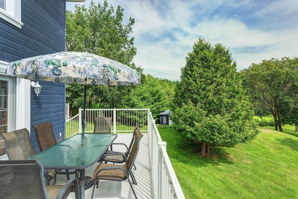 A patio with a glass table and chairs, an umbrella, and a small deck area.