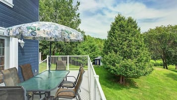 A patio with a glass table and chairs, an umbrella, and a small deck area.