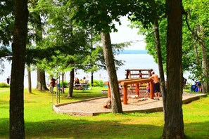Un parc amb un parc infantil, taules de picnic i un llac al fons.