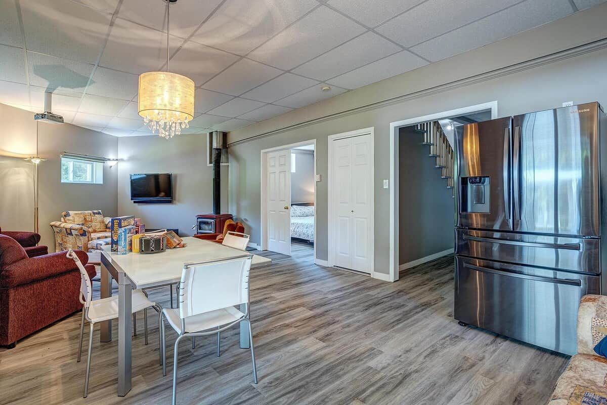 A modern kitchen with a stainless steel refrigerator, a dining table with chairs, and a chandelier.