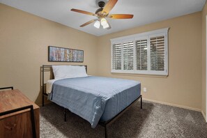 A bedroom with a bed, a ceiling fan, a window with shutters, and a painting on the wall. - El Paso Desert Oasis (El Paso)