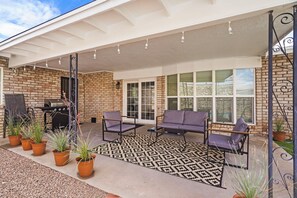 A covered patio with a brick wall, a grill, two purple chairs, and potted plants. - El Paso Desert Oasis (El Paso)