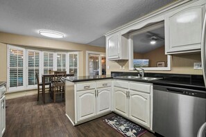 A modern kitchen with white cabinets, a stainless steel dishwasher, and a dining area with a table and chairs. - El Paso Desert Oasis (El Paso)