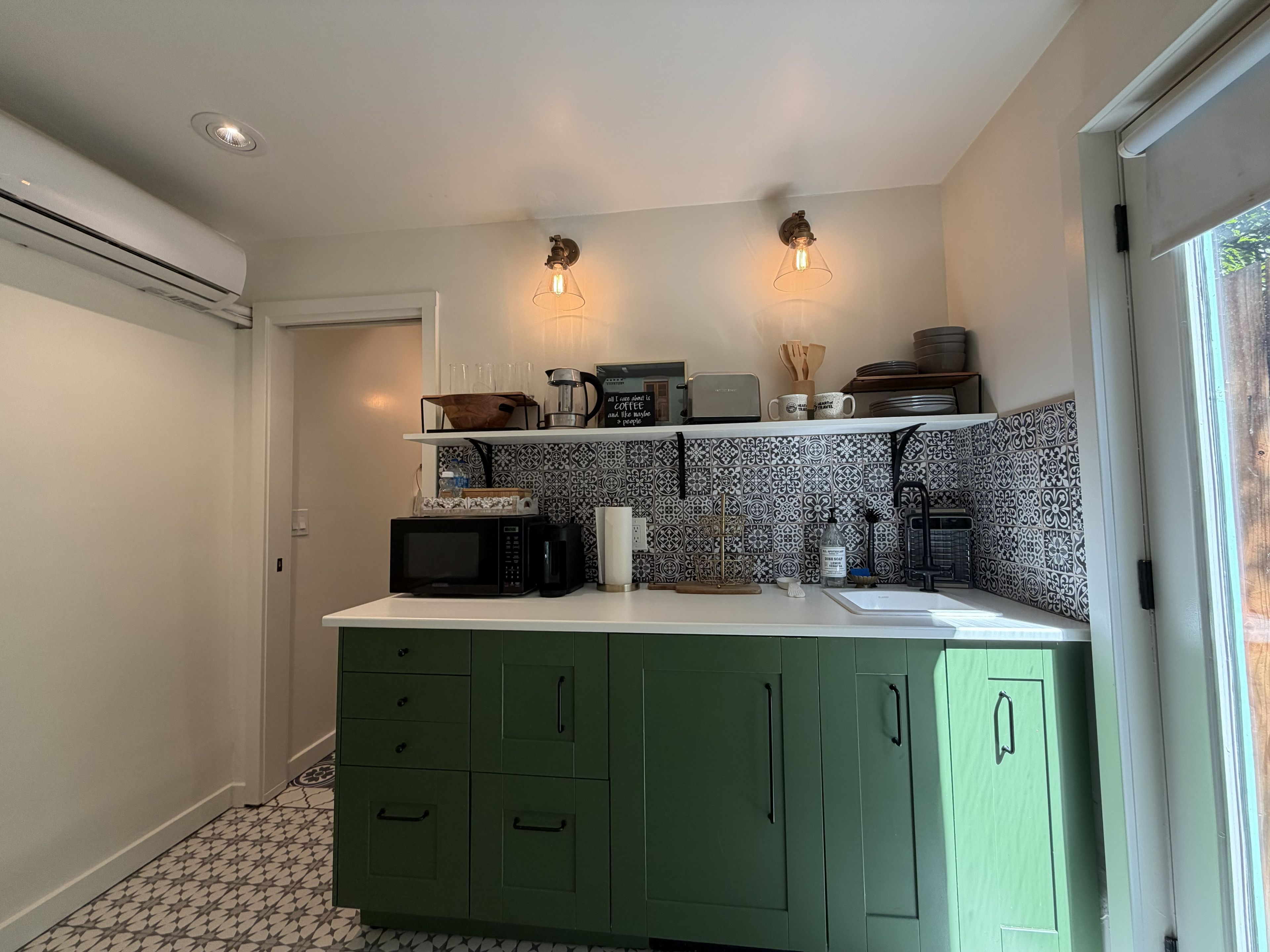 A compact kitchen with green cabinets, a microwave, a coffee maker, and two wall-mounted light fixtures.
