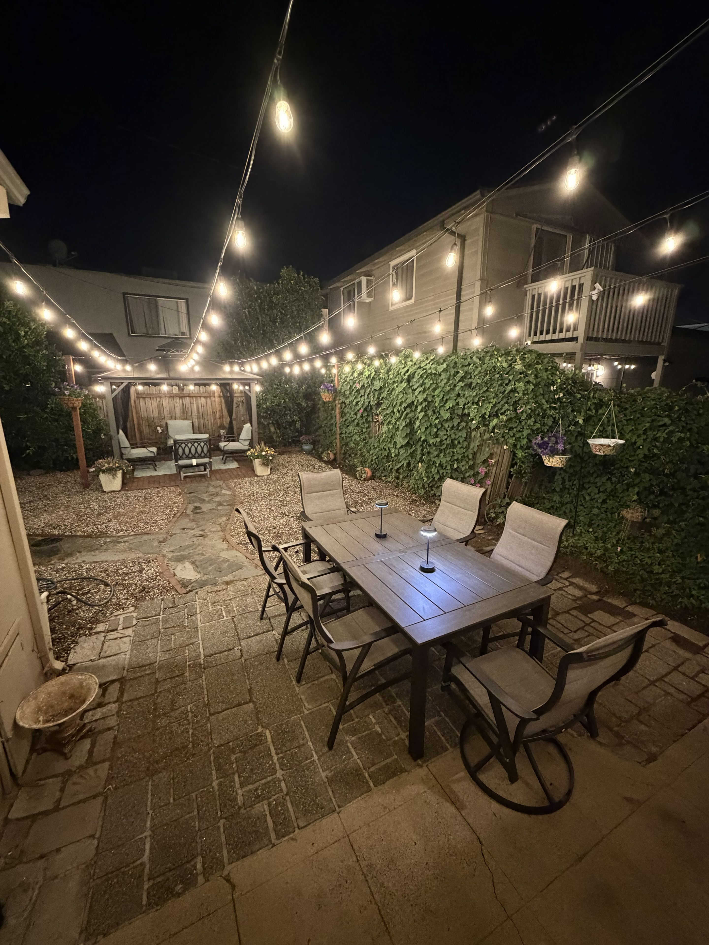 An outdoor patio with a table and chairs, string lights, and a house in the background.