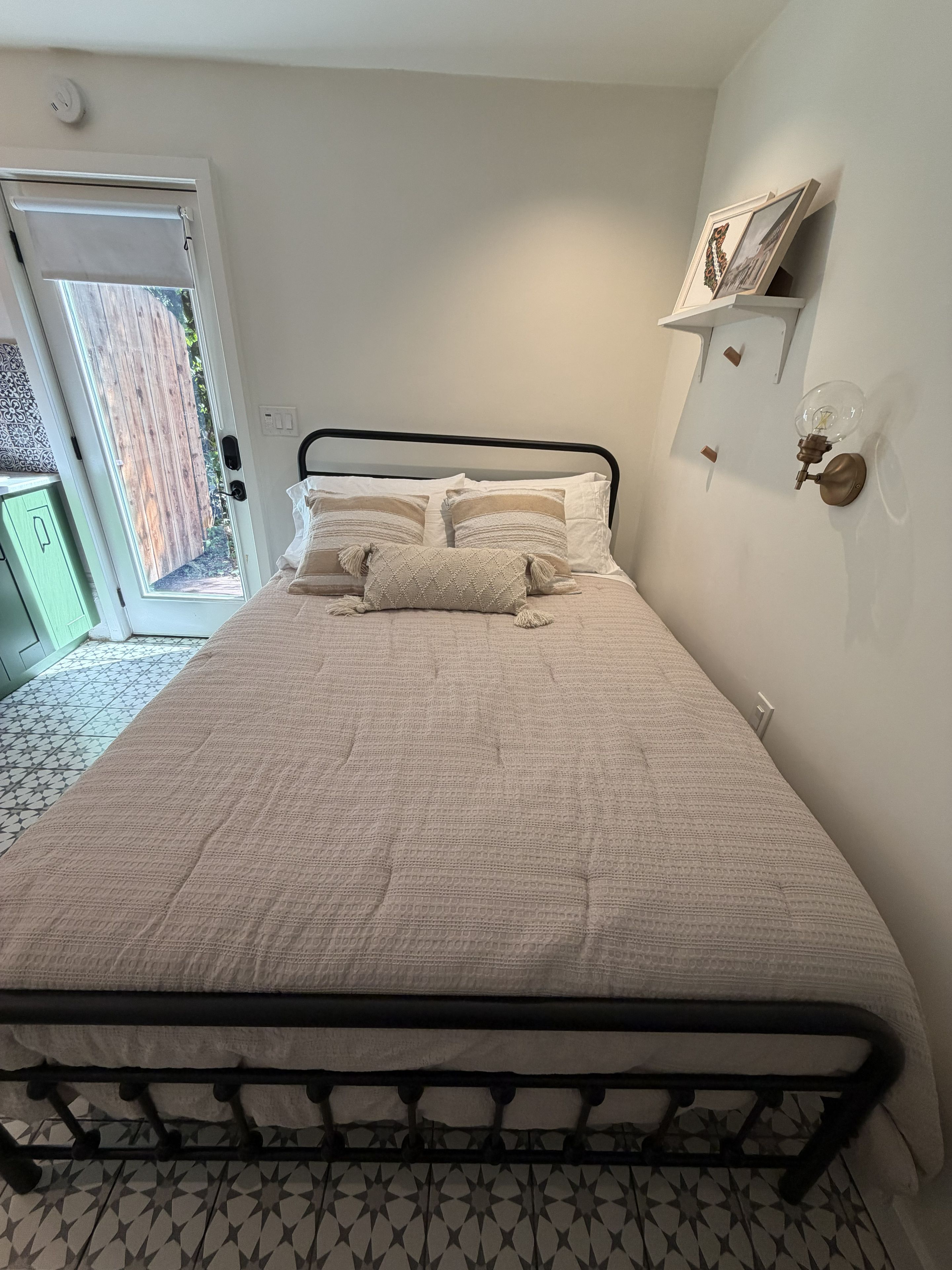 Uma cama com colcha estampada, um travesseiro e uma luminária fixada na parede.