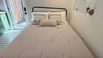 Uma cama com colcha estampada, um travesseiro e uma luminária fixada na parede.
