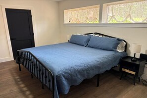 Un dormitori amb llit, una tauleta de nit, una porta i finestres amb cortines.