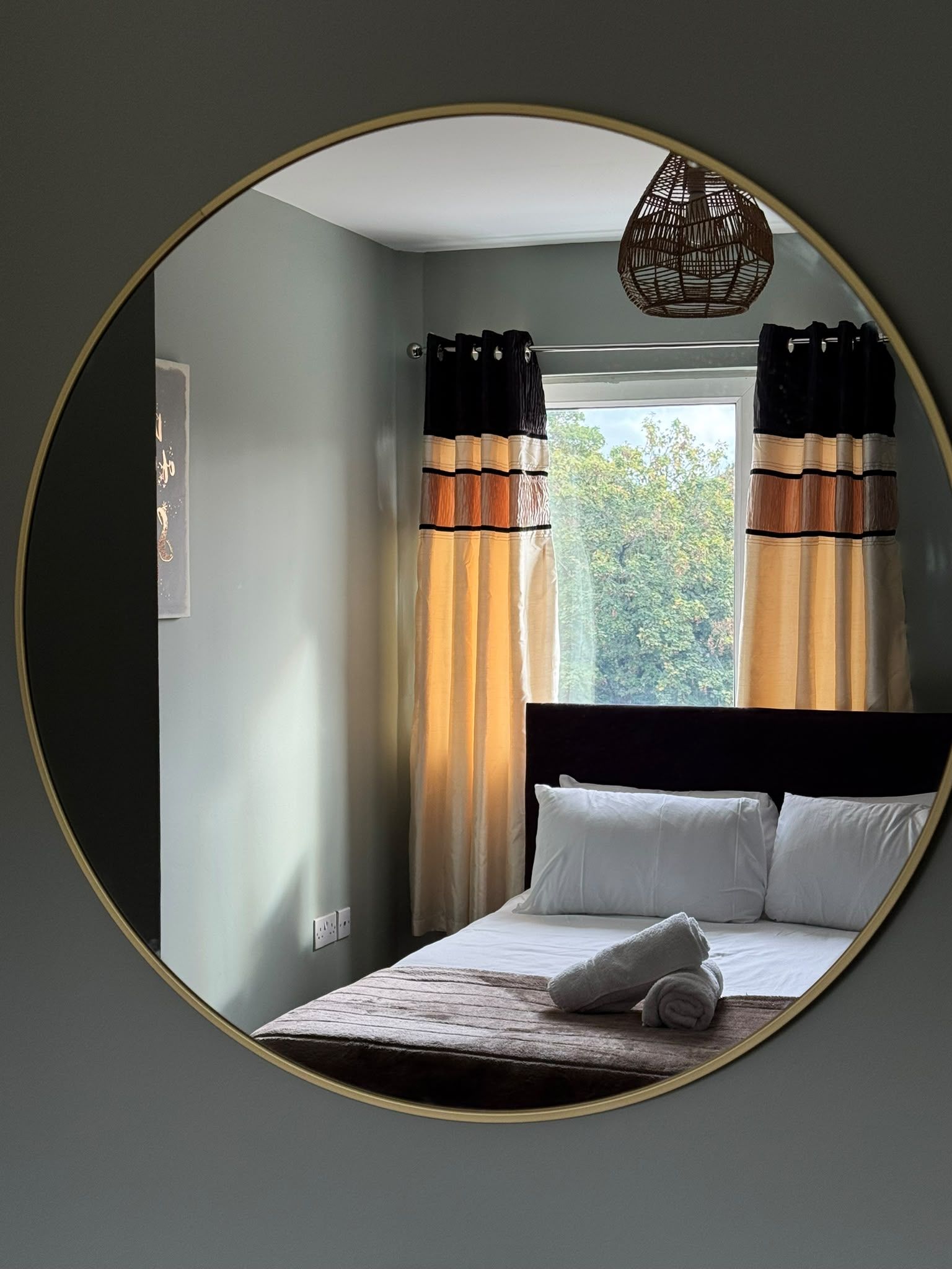 Een slaapkamer met een bed, gordijnen, een raam en een wandlamp.
