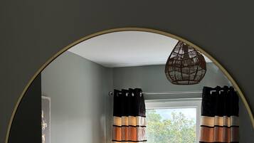 Een slaapkamer met een bed, gordijnen, een raam en een wandlamp.
