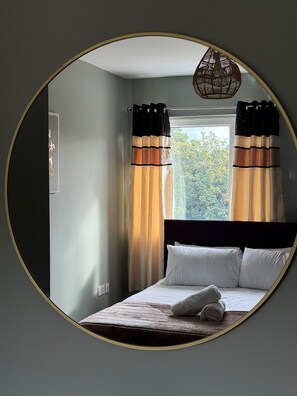 Un dormitorio con cama, cortinas, una ventana y una lámpara fijada a la pared.