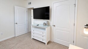 A room with a white dresser, a flat-screen TV mounted above it, and two closed white doors. - Spacious 5BR Solterra Retreat with Private Pool (Davenport)