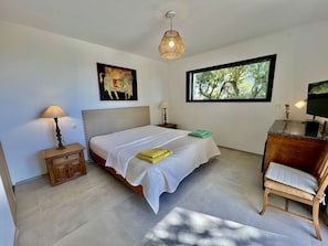 A bedroom with a bed, bedside lamps, a desk with a chair, a window with a view, and artwork on the wall. - VILLA NEAR THE BEACH WITH SWIMMING POOL AND LOVELY SEA VIEWS TO RENT FOR 10 PEOPLE (STE MAXIME)