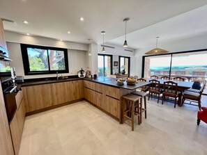 A modern kitchen with a large island, wooden cabinets, and a view of the ocean. - VILLA NEAR THE BEACH WITH SWIMMING POOL AND LOVELY SEA VIEWS TO RENT FOR 10 PEOPLE (STE MAXIME)