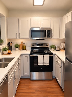 A modern kitchen with stainless steel appliances, white cabinetry, and a wooden floor. - The Varsity Suite w/ Community Gym & Pool! (Athens)