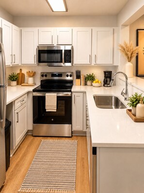A modern kitchen with white cabinets, stainless steel appliances, and a central island with a sink. - Red Zone Suite w/ Free Shuttle! (Athens)