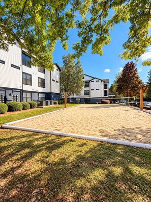 A modern building with a flat roof, multiple windows, and a paved area with a volleyball net. - Red Zone Suite w/ Free Shuttle! (Athens)