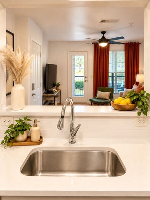 A modern kitchen with a stainless steel sink, a ceiling fan, and a view of the outdoors through a sliding glass door. - Red Zone Suite w/ Free Shuttle! (Athens)