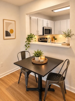 A modern kitchen with white cabinets, a microwave, and a built-in oven. There is a dining table with chairs and a candle on a tray. - The Athens Playbook w/ Pool & Shuttle! (Athens)