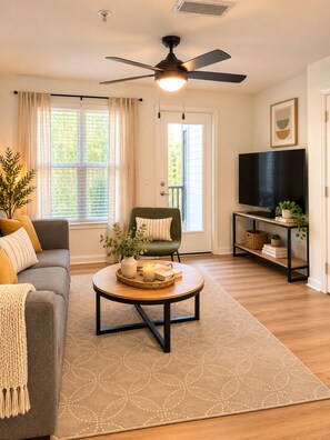 Ein Wohnzimmer mit einer Couch, einem Couchtisch, einem Fernseher und einem Deckenventilator.