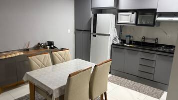 A modern kitchen with grey cabinets, a white refrigerator, a microwave, and a gas stove. There is a dining table with chairs and a rug on the floor.