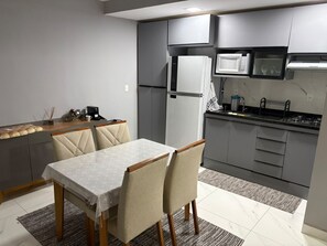 Una cocina moderna con armarios grises, un refrigerador blanco, un microondas y una estufa a gas. Hay una mesa de comedor con sillas y una alfombra en el suelo.