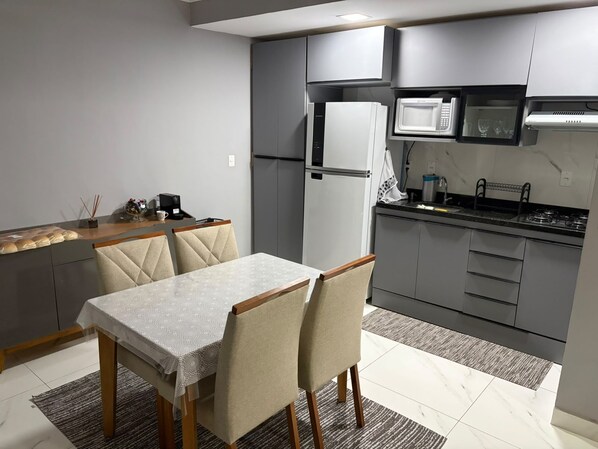 Eine moderne Küche mit grauen Schränken, einem weißen Kühlschrank, einer Mikrowelle und einem Gasherd. Ein Esstisch mit Stühlen und ein Teppich sind auf dem Boden.