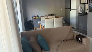 A living room with a beige sofa, a ceiling fan, and a kitchen area with a microwave and refrigerator.