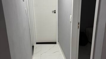 A narrow hallway with white tiled walls and a white door with a black doorknob.