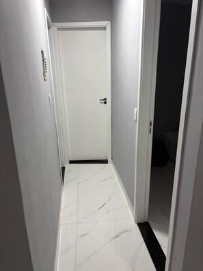 Ein schmaler Flur mit weißen Fliesenwänden und einer weißen Tür mit schwarzem Drücker.
