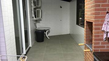 A small, enclosed patio area with a tiled floor, a brick oven, and a small table with a chair.