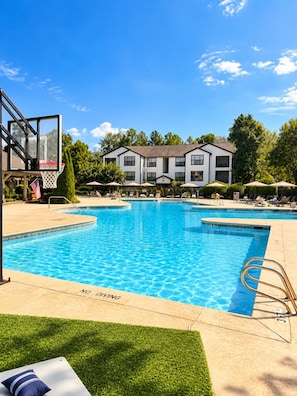 A swimming pool with a basketball hoop, lounge chairs, and a building in the background. - Classic City Clubhouse w/ Community Pool (Athens)