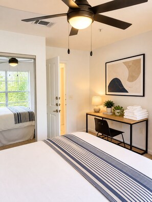 A hotel room with a bed, a desk with a lamp, a ceiling fan, and a window with blinds. - The Athens All-Star w/ Free Shuttle (Athens)