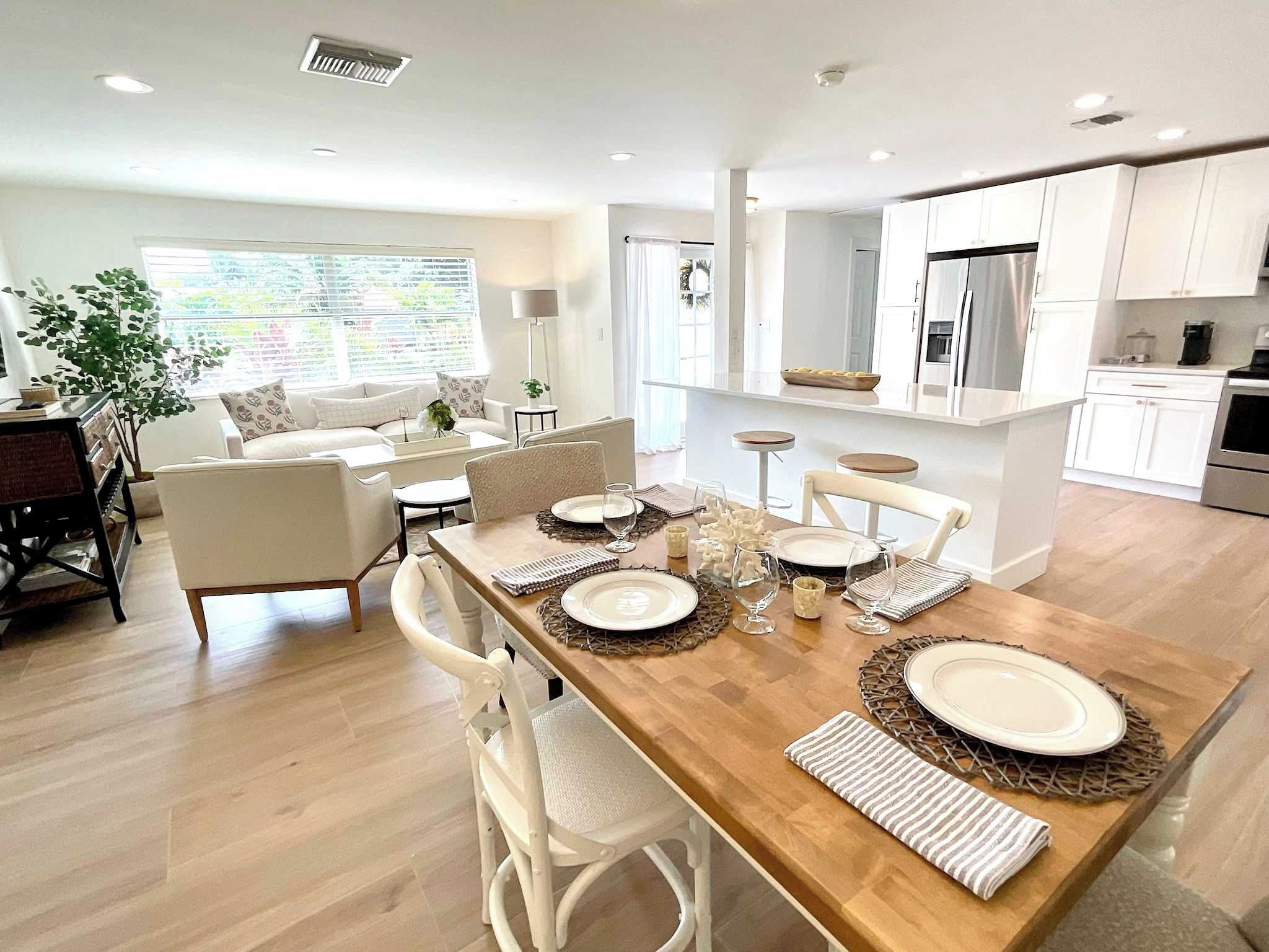 A modern kitchen with white cabinets, a central island, and a dining area with white chairs and a wooden table.