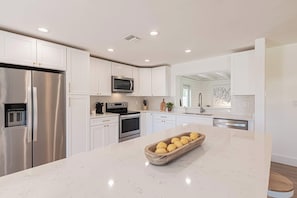 A modern kitchen with white cabinetry, stainless steel appliances, and a marble countertop. - New Vacation Pool Home, 3 BD, Minutes from Beach! (Naples)